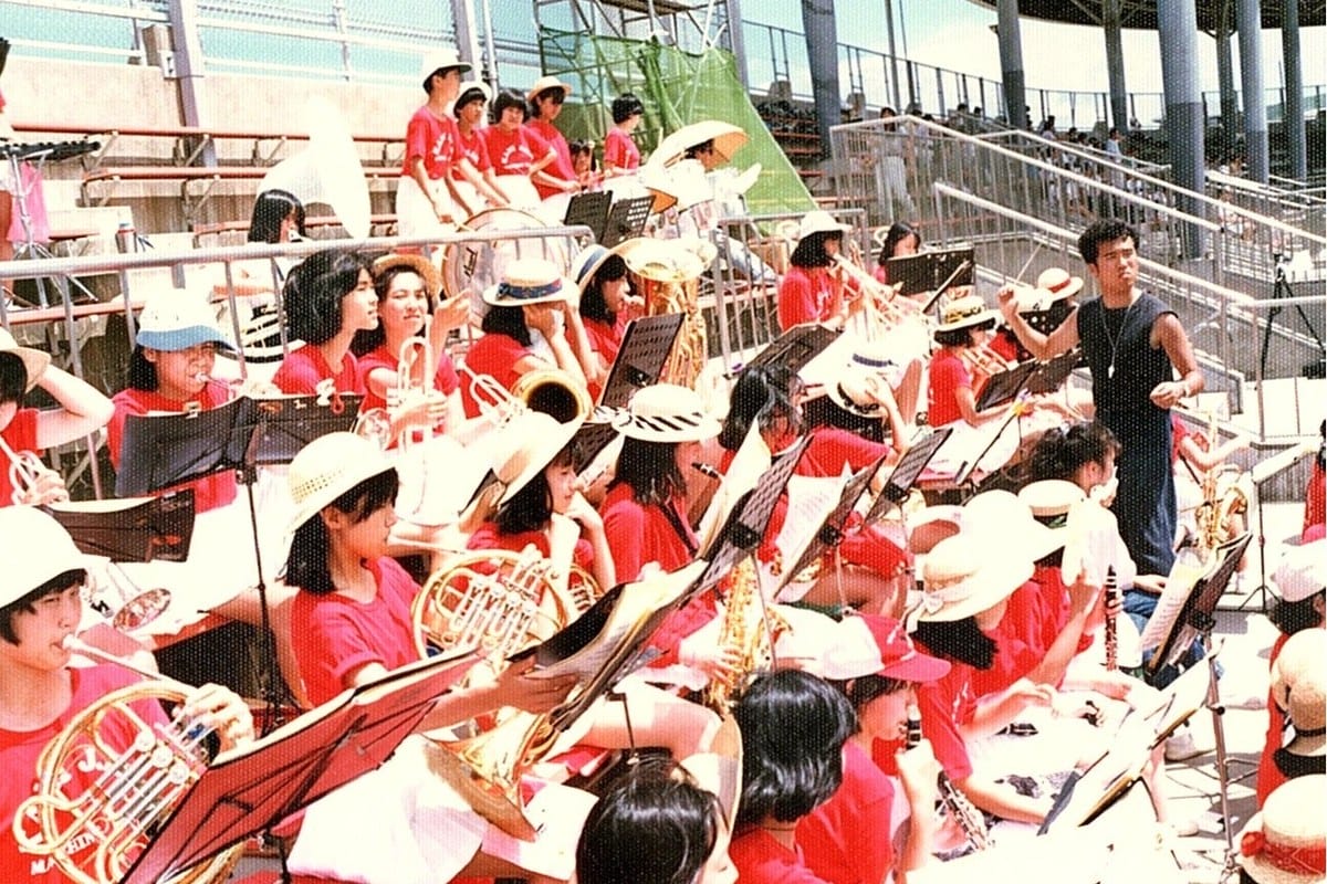 アルプス席で赤いTシャツの吹奏楽部員たちが金管楽器を奏でている様子。